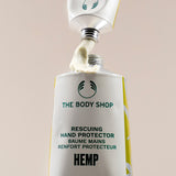 The Body Shop hand protector with cream being applied on a beige background