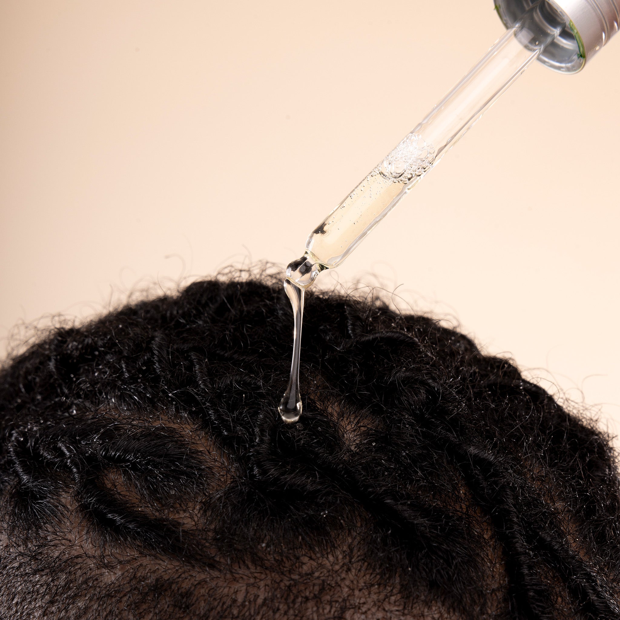 Bottle of The Body Shop Scalp Serum being dripped onto braided hair against a beige background