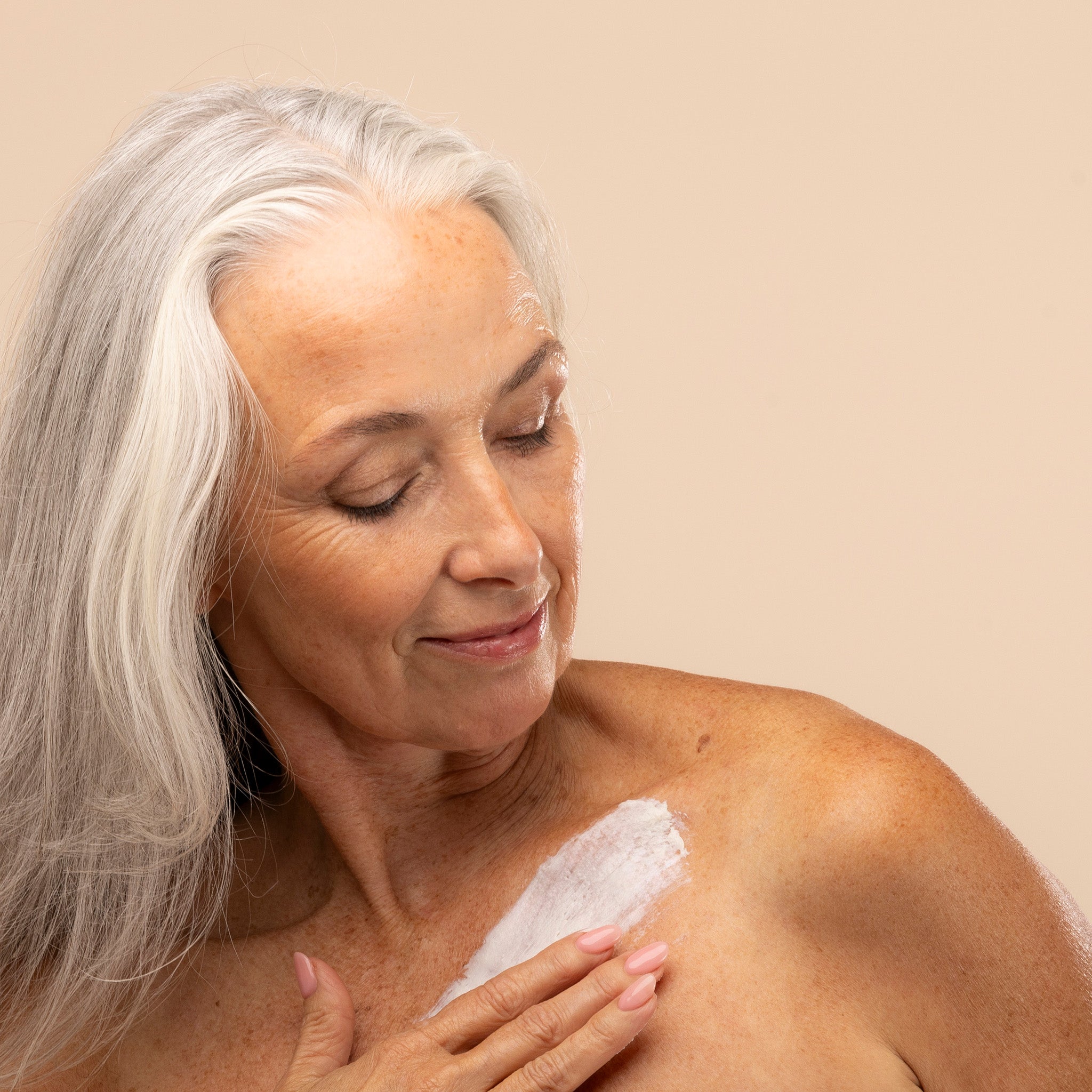 Woman applying shea body butter to her shoulder against a beige background