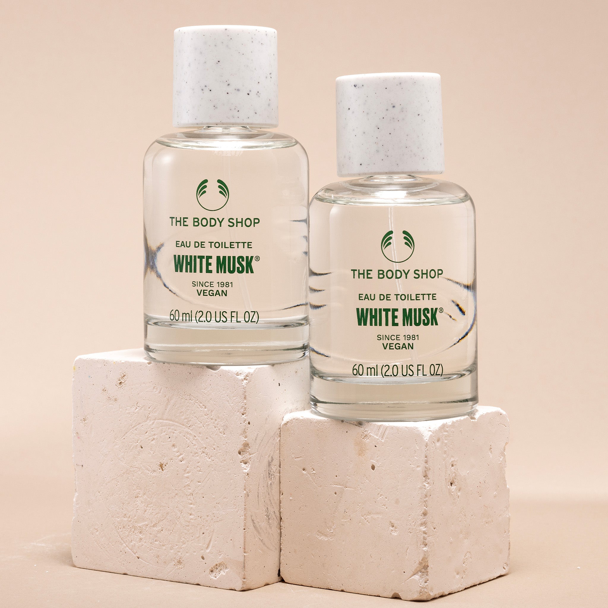 Two bottles of The Body Shop White Musk eau de toilette on beige blocks with a beige background.