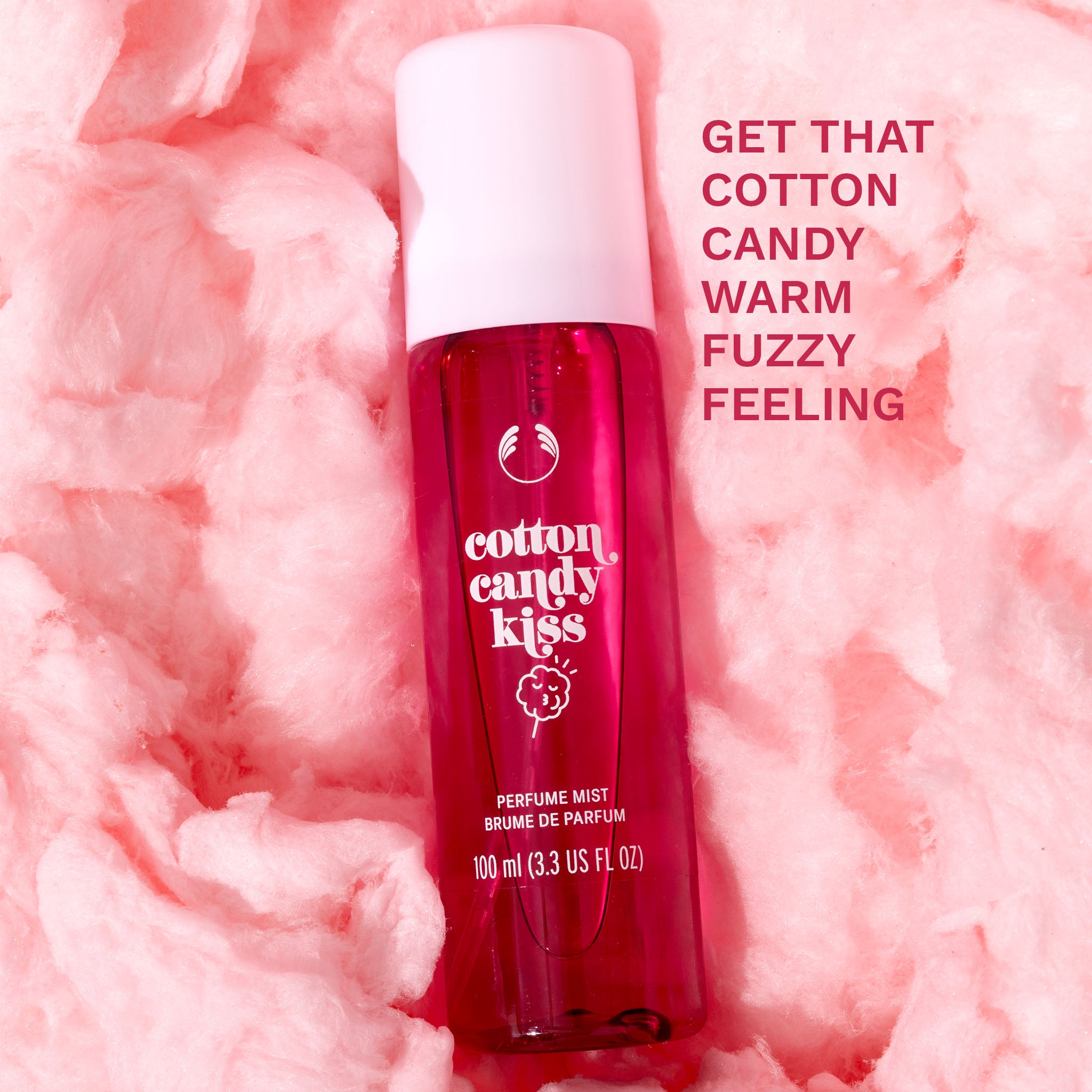 Cotton Candy Kiss fragrance mist - The Body Shop. Bottle lying on a bed of cotton candy. Overlay text 'Get that cotton candy warm fuzzy feeling'.